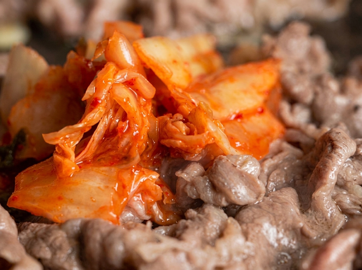Un mucchio di kimchi rosso vivo mescolato a straccetti di manzo a fette sottili in una padella.