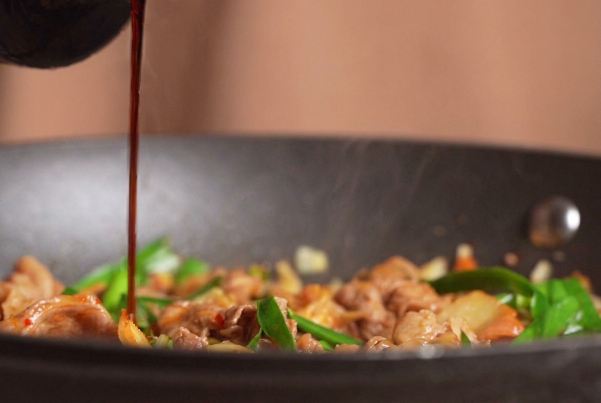 Salsa di soia scura versata da una bottiglia su un fumante piatto di manzo, kimchi ed erba cipollina saltati in padella.