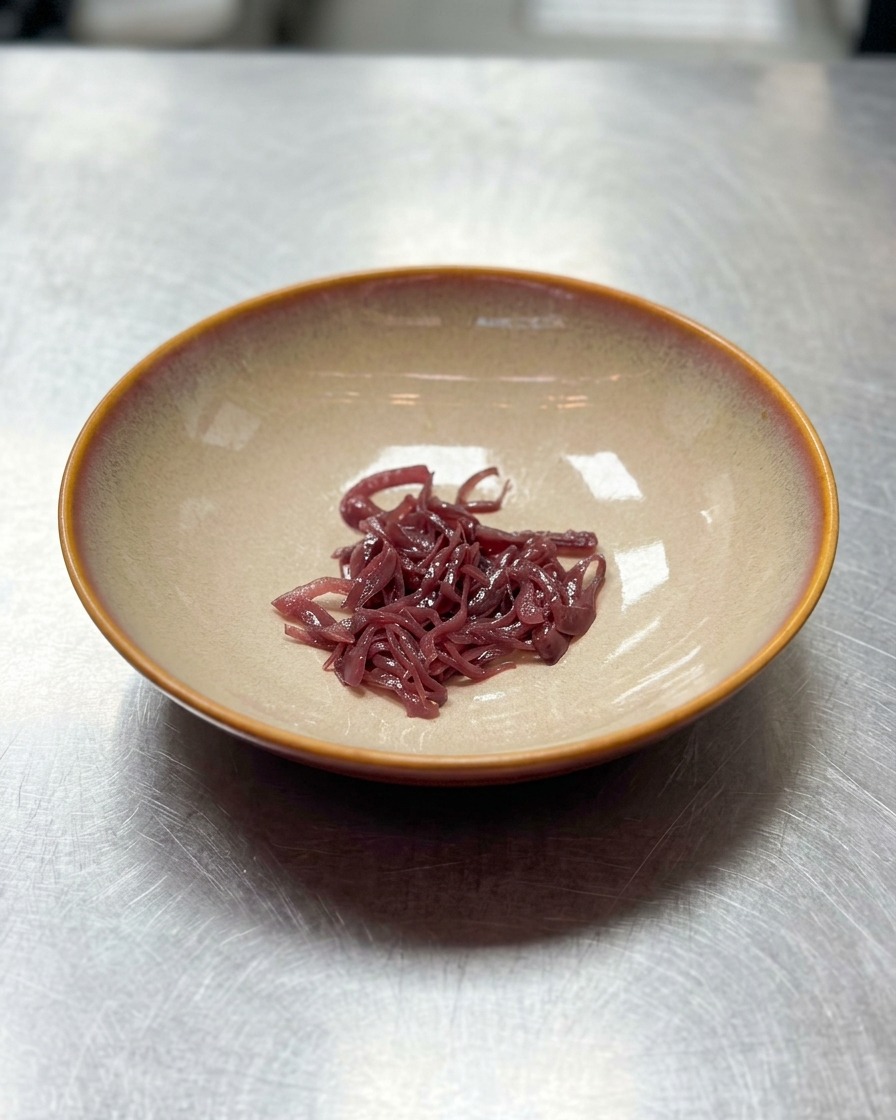 Una piccola manciata di cipolle rosse tagliate a striscioline posizionata al centro di una ciotola di ceramica beige vuota.