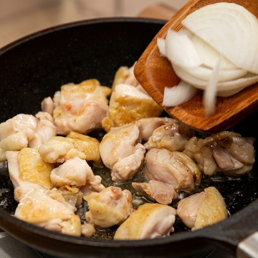 Cipolle bianche affettate finemente trasferite da una spatola di legno a una padella con il pollo rosolato.