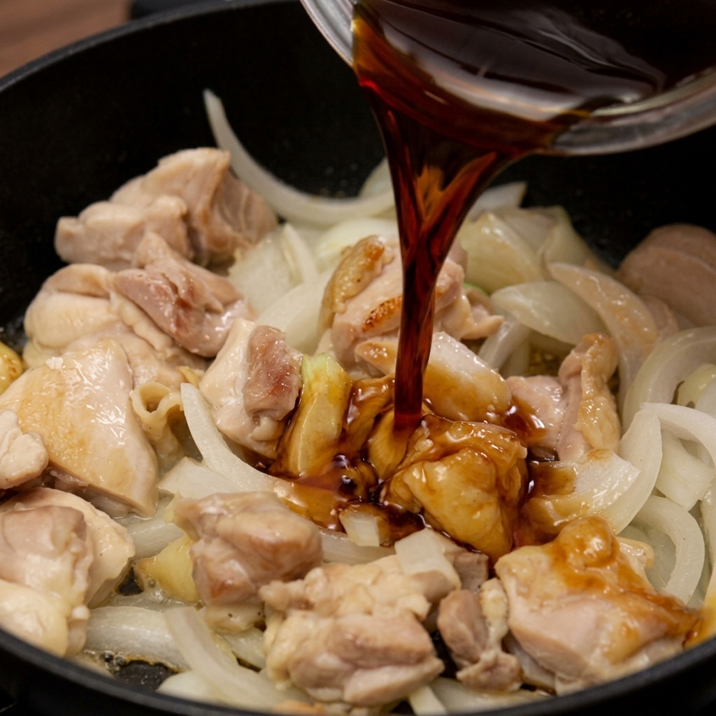 Una salsa scura a base di soia viene versata in una padella con pollo saltato e cipolle bianche.