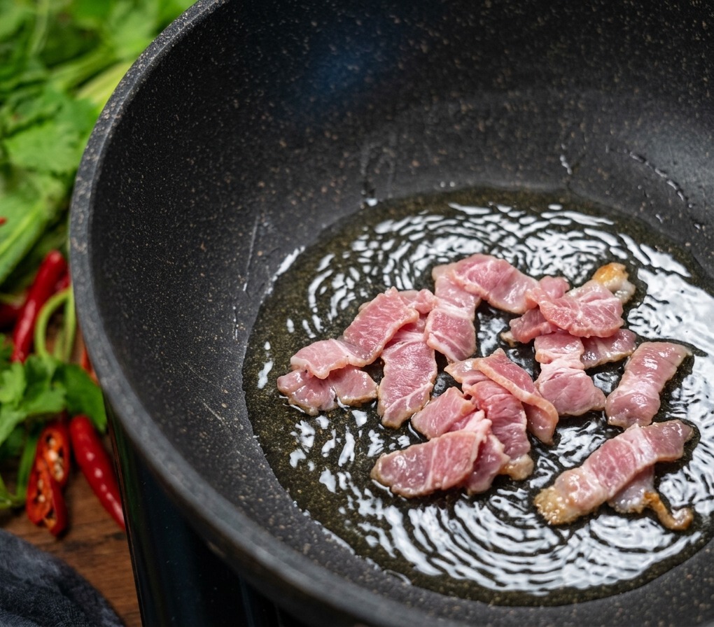 Pezzetti di bacon che sfrigolano in una padella antiaderente scura, con bollicine che si formano nel grasso sciolto mentre la carne si dora.