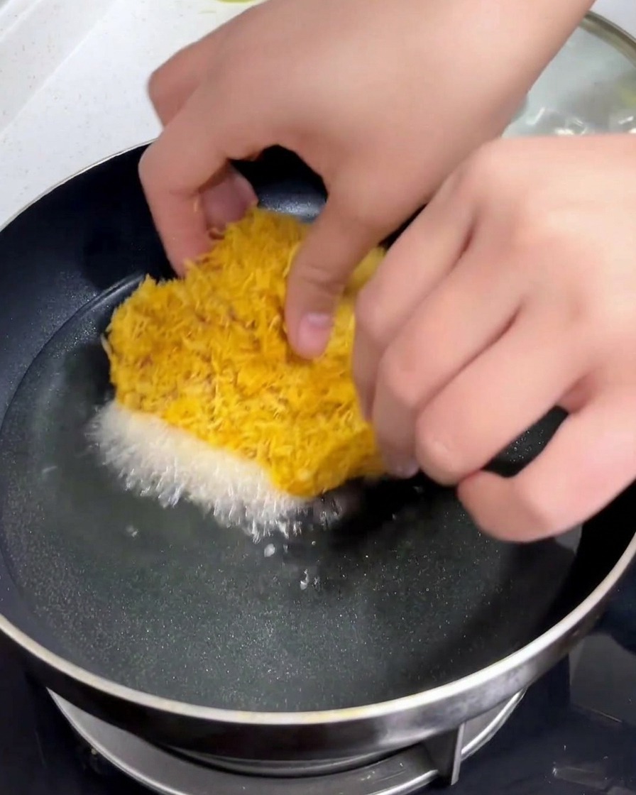 Una cotoletta di maiale impanata viene calata a mano in una padella di olio caldo e sfrigolante.