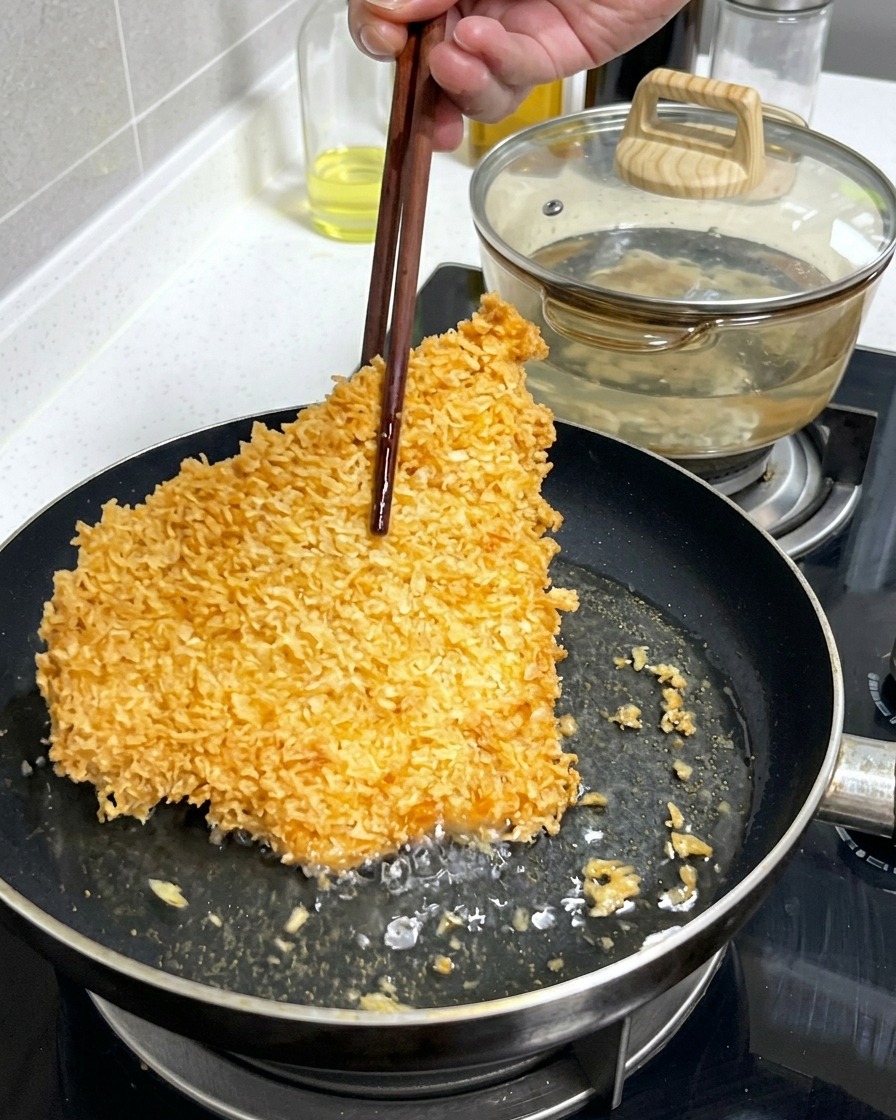 Una grande cotoletta di maiale impanata, dorata e croccante, viene sollevata o girata con bacchette di legno in una padella con olio bollente.