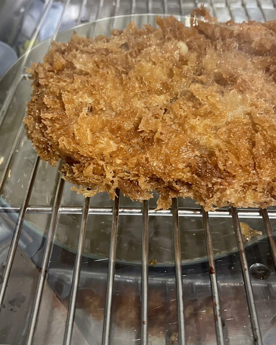 Un primo piano di una cotoletta di maiale fritta coperta da una croccante e frastagliata panatura di panko, adagiata su una griglia metallica.