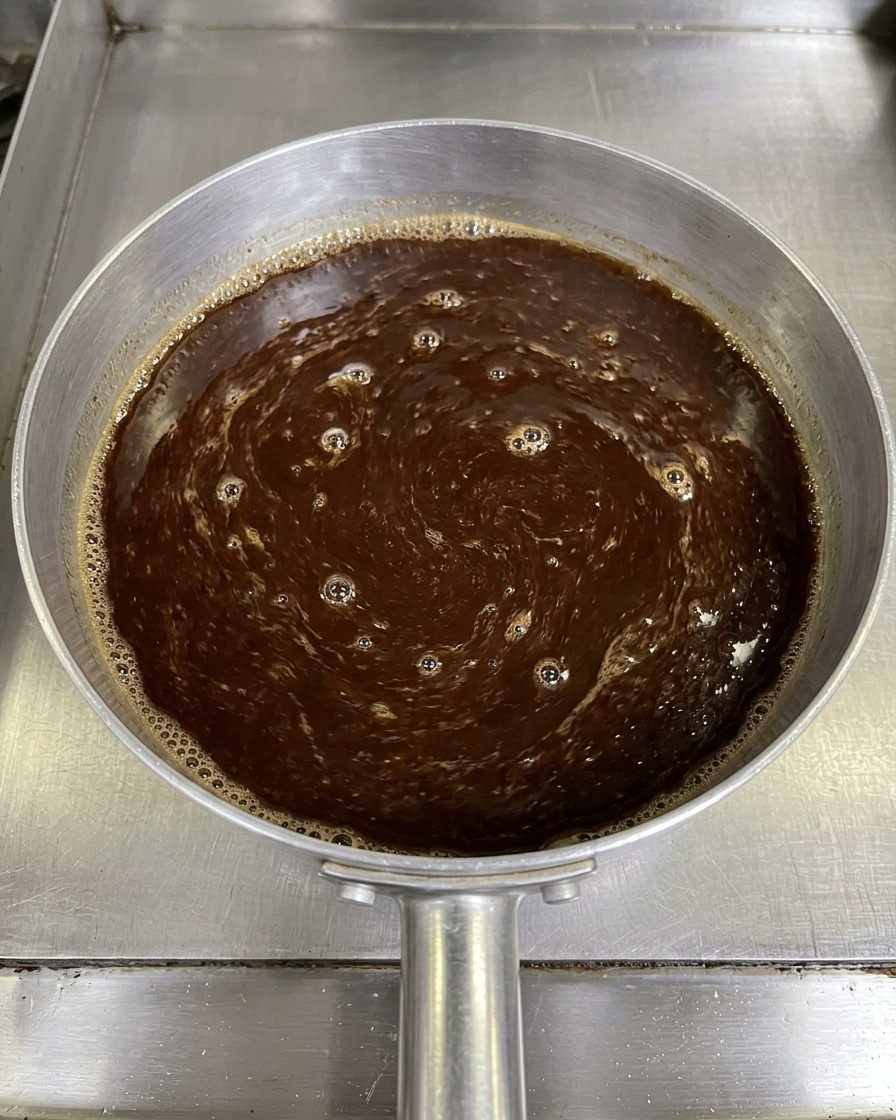 Una vista dallalto di una miscela scura di salsa al miso mescolata con un paio di bacchette in un piccolo pentolino di alluminio.