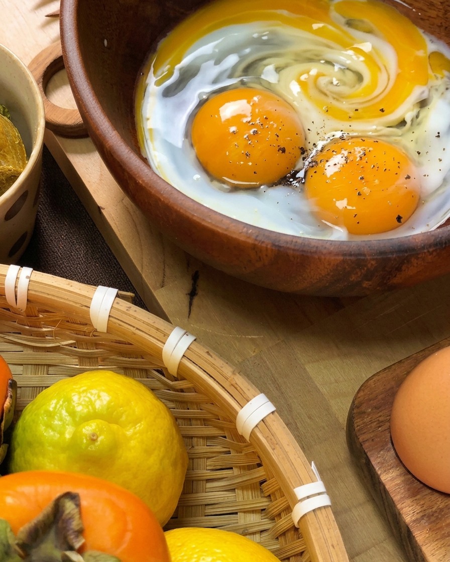 Uova fresche aperte in una ciotola di legno con pepe nero e un goccio di latte, pronte per essere sbattute.