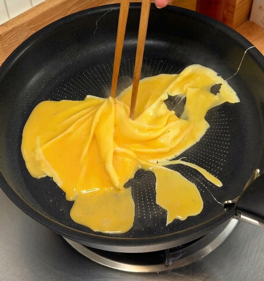 Bacchette che girano unomelette parzialmente cotta in una padella antiaderente nera per creare un motivo a spirale.