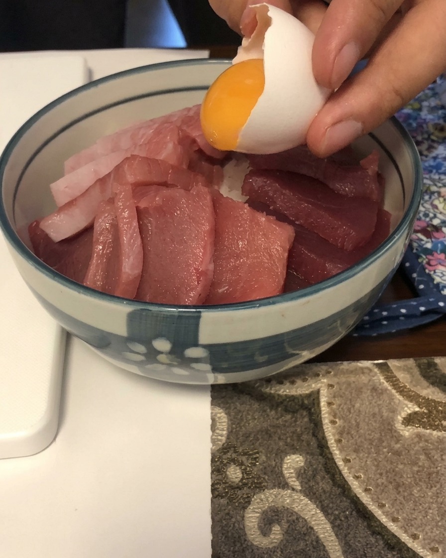 Un tuorlo duovo giallo brillante scivola fuori da un guscio bianco su un letto di pesce crudo a fette in una ciotola bianca e blu.