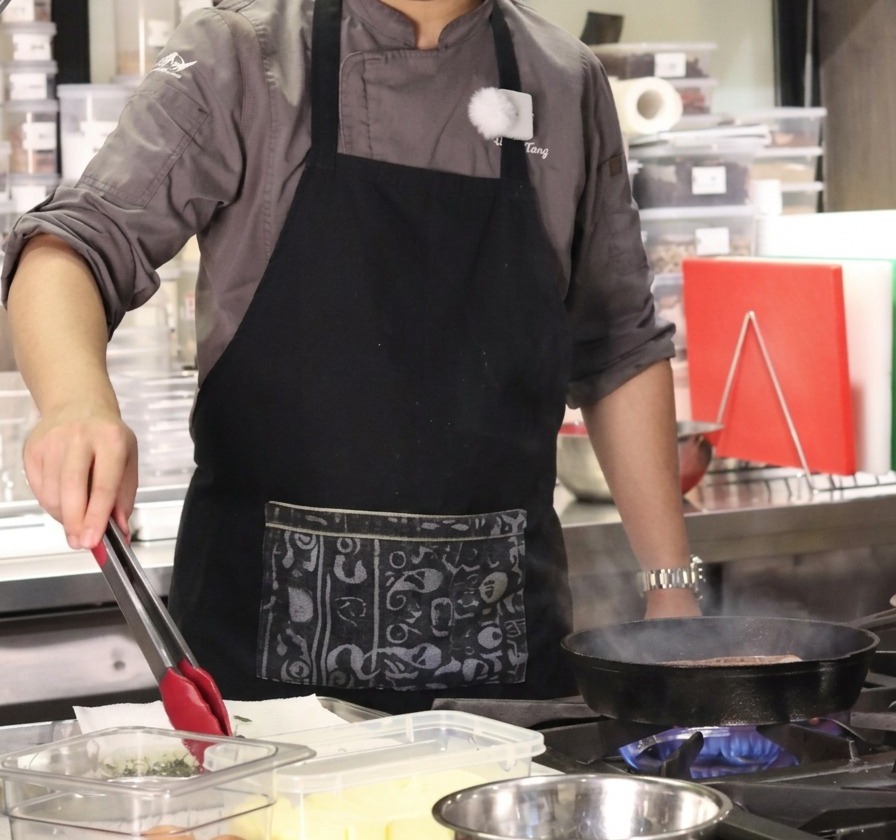 Lo chef usa le pinze per trasferire rametti di timo fresco e aglio da un contenitore alla padella.