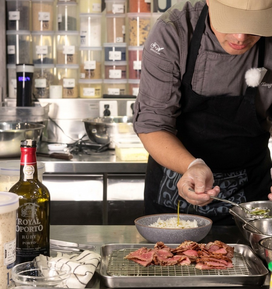 Uno chef versa un cucchiaino di olio di cipollotto limpido su una ciotola di riso bianco, con il manzo affettato che riposa su una griglia vicina.