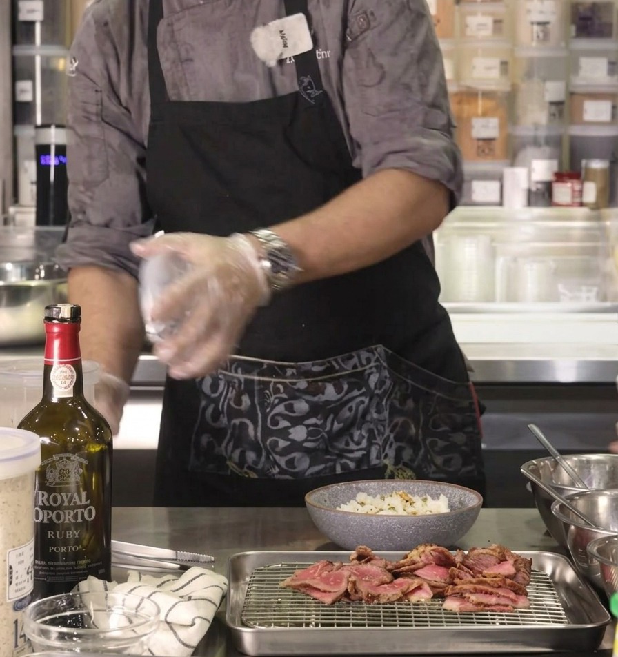 La mano dello chef che spolvera del saporito condimento furikake su una ciotola di riso posizionata su un bancone da cucina in acciaio inox.
