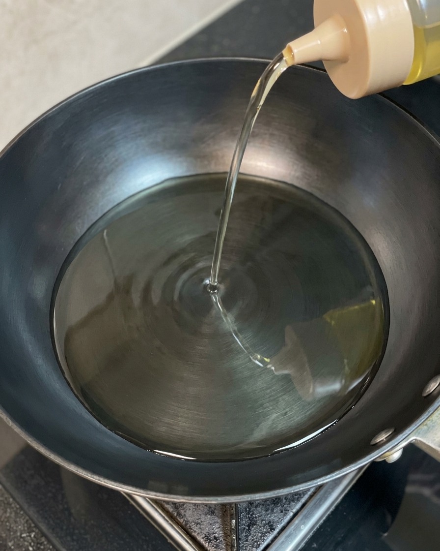 Olio di semi limpido versato da una bottiglia dosatrice in un wok scuro e ben caldo.