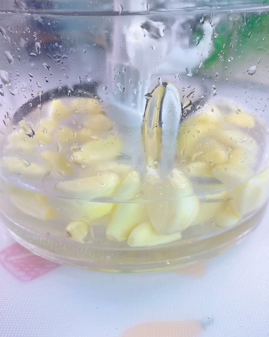 Spicchi daglio sbucciati e sale immersi in acqua allinterno del bicchiere di un frullatore trasparente.