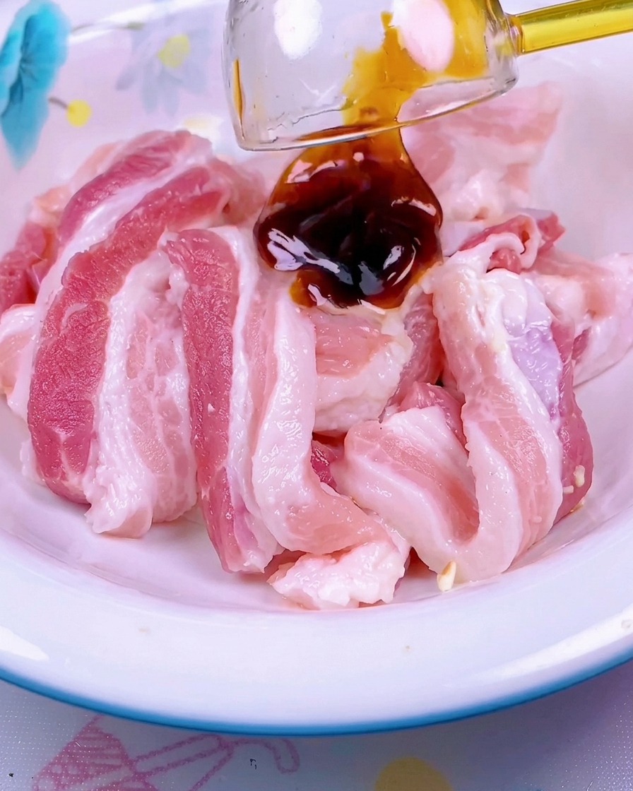 Una salsa rosso scuro viene versata sopra le fette di pancetta di maiale cruda in una ciotola di ceramica bianca.
