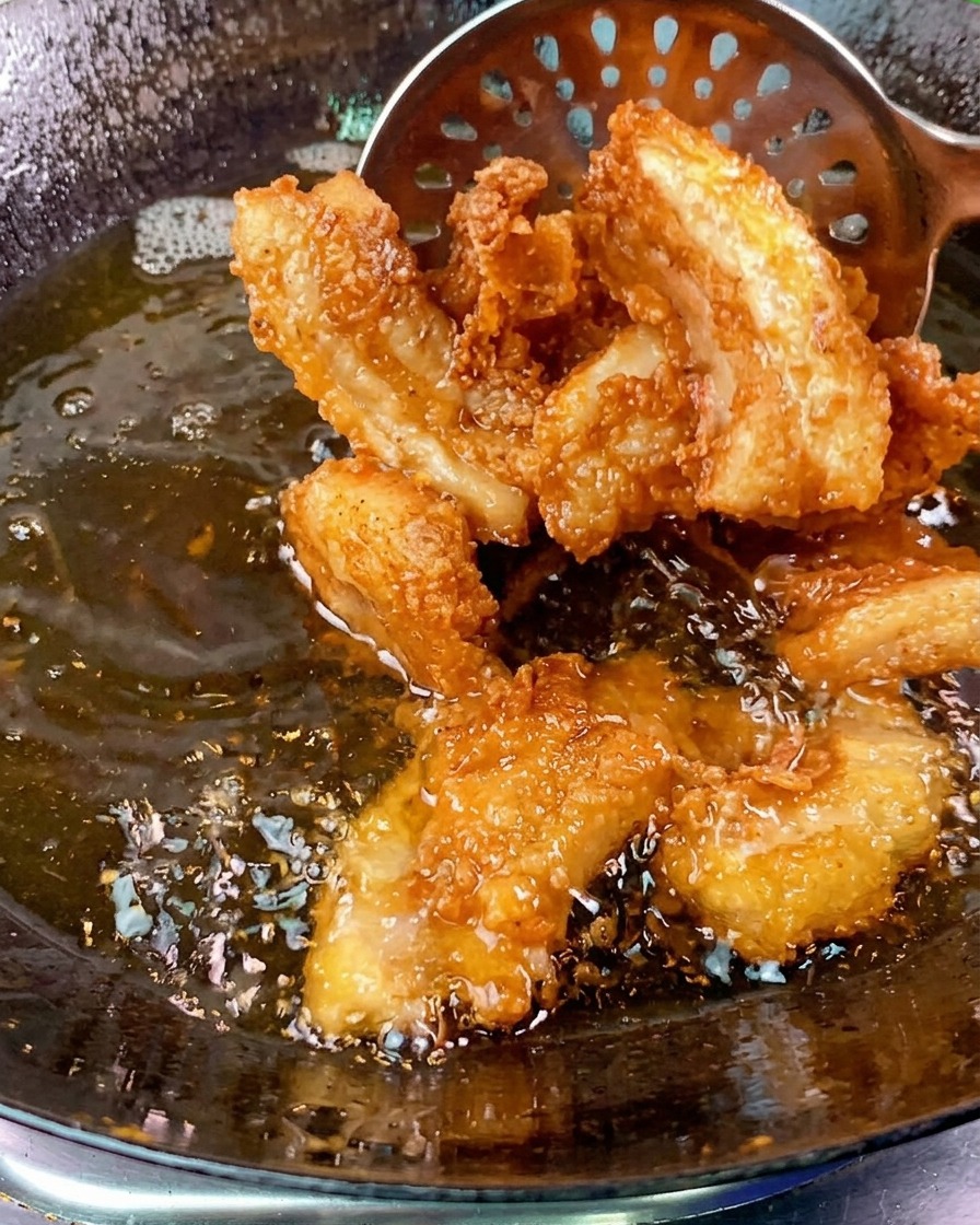 Fette di pancetta dorate e croccanti vengono sollevate da un wok dolio bollente con una schiumarola di metallo.