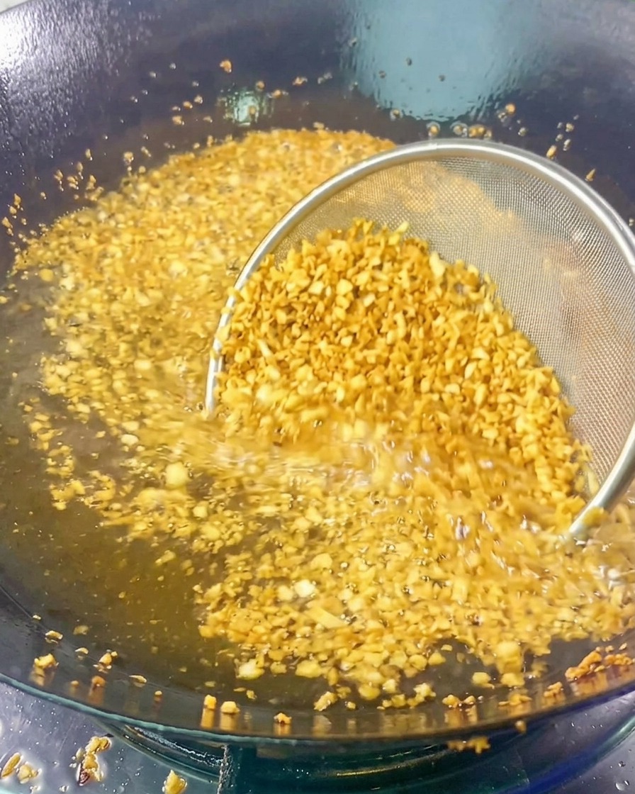 Un colino a maglia fine pieno di aglio tritato viene immerso nellolio bollente mentre diventa dorato e profumato.