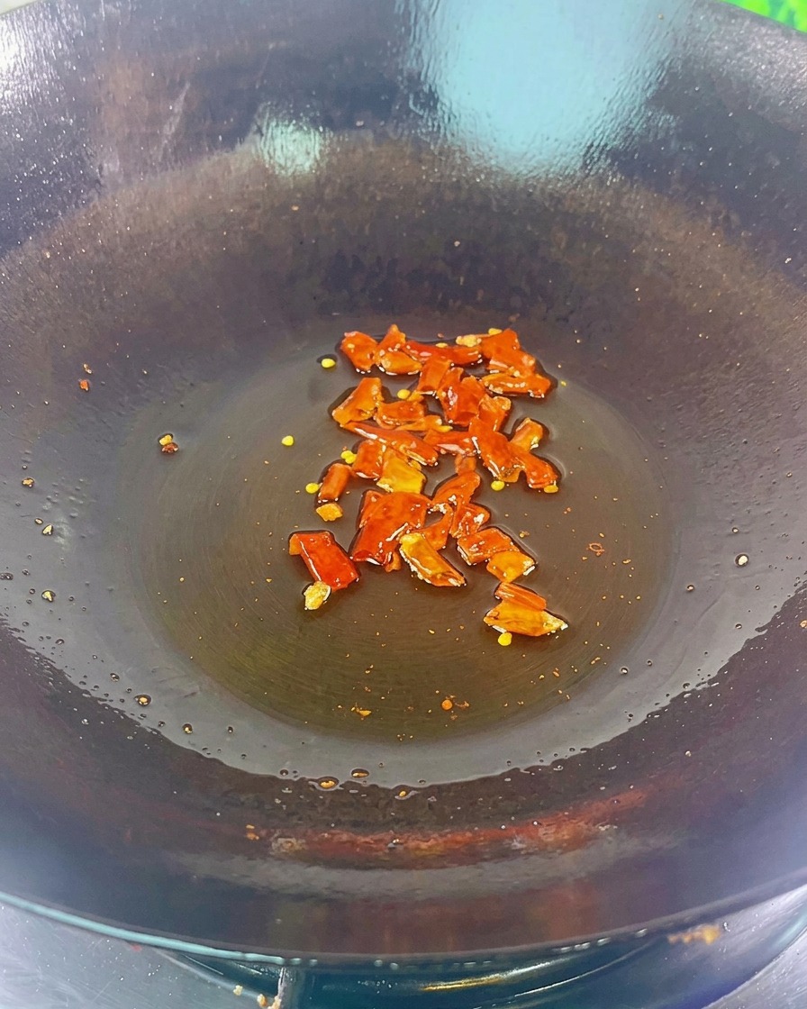 Pezzi di peperoncino rosso secco e fagioli neri sfrigolano sul fondo di un wok scuro con un velo dolio.