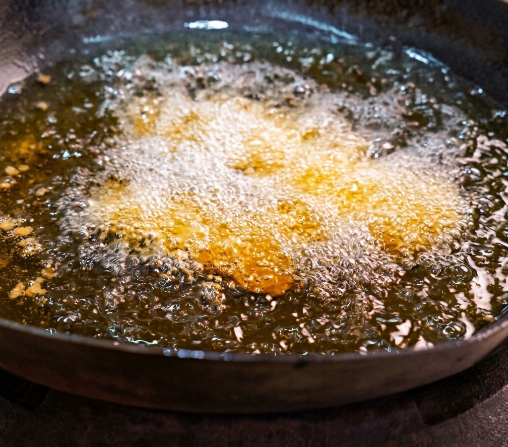 Fette di pancetta di maiale marinata che friggono in un wok pieno di olio caldo e spumeggiante.