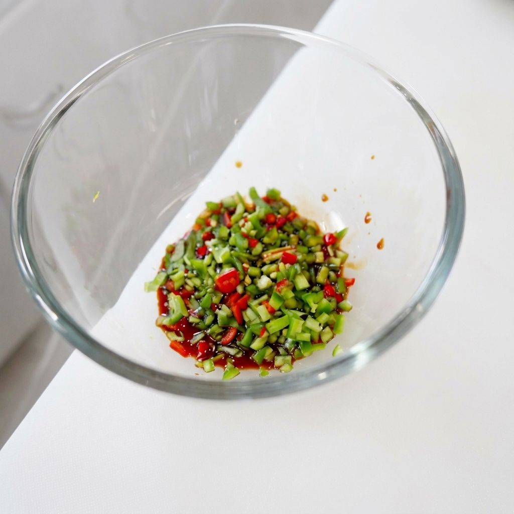 Un mix vivace di coriandolo e peperoncini verdi e rossi tritati finemente immersi in una base liquida scura e lucida allinterno di una ciotola di vetro.