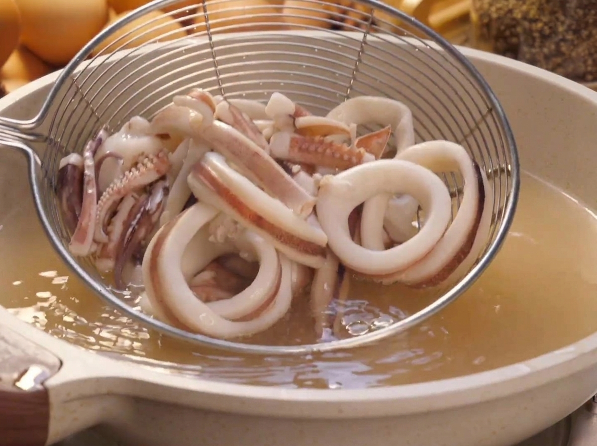 Una schiumarola a maglia fine che solleva gli anelli di calamaro sbollentati dalla pentola dacqua bollente.