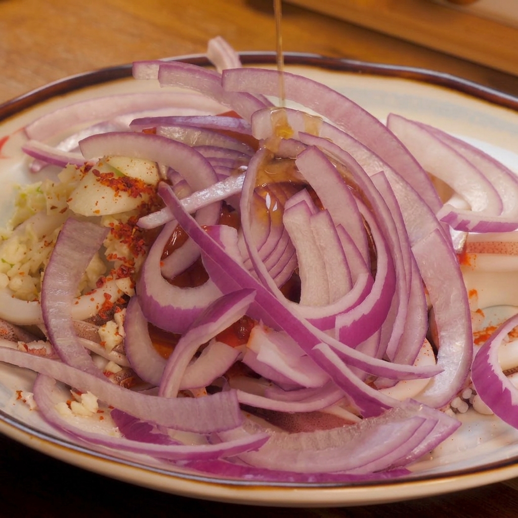 Un filo di olio di sesamo limpido versato dallalto su una colorata montagnola di cipolle rosse, peperoncino e calamari.