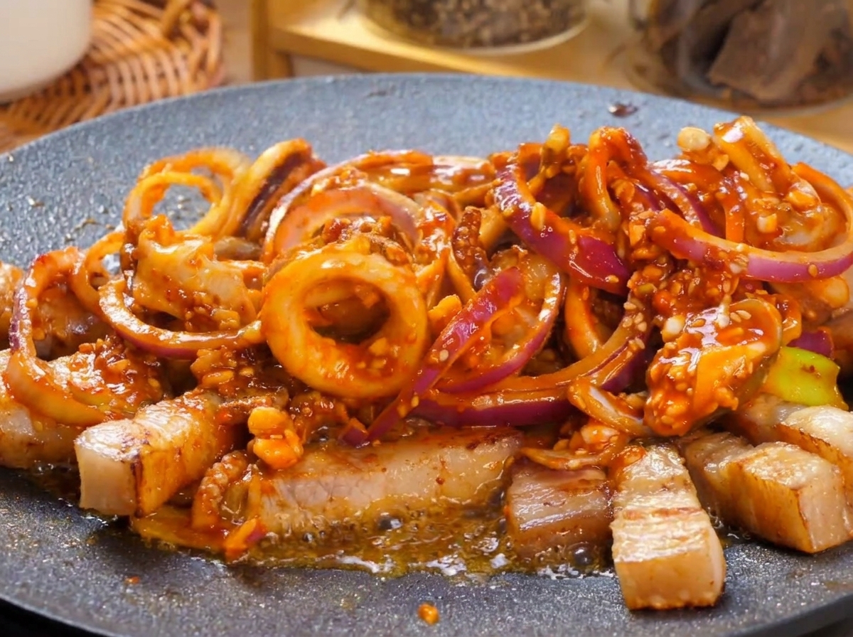 Una piastra bollente con calamari e pancetta in salsa piccante che sobbolle vigorosamente, guarnita con rondelle di peperoncino verde fresco.