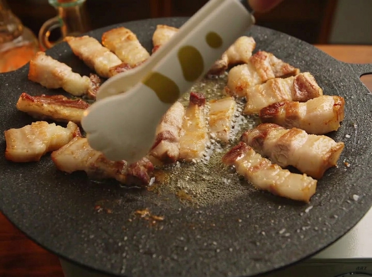 Una pinza che sistema i bocconcini di pancetta grigliata in cerchio lungo il bordo di una piastra di ghisa nera.