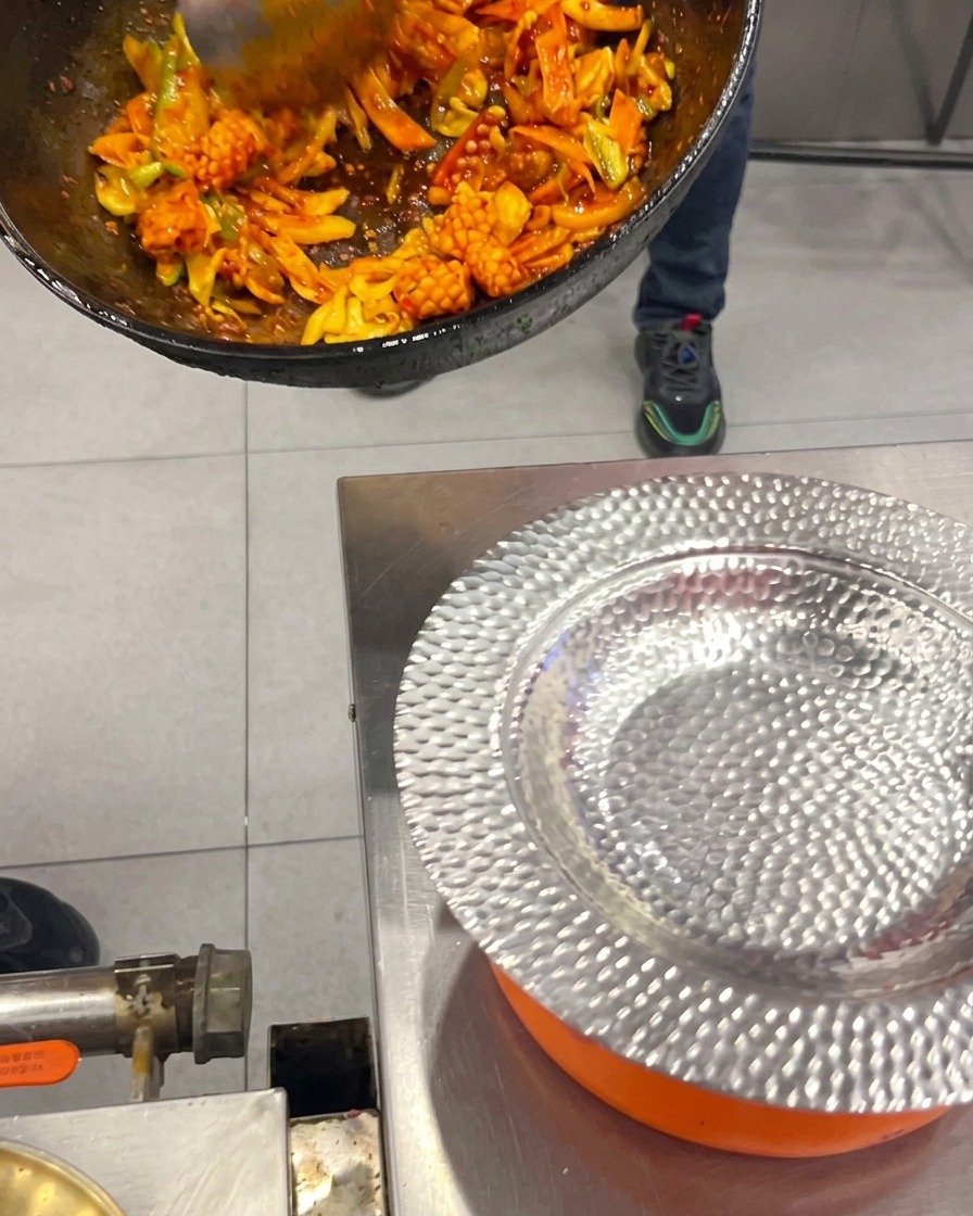 Calamari e pancetta piccanti alla coreana saltati con verdure che vengono raccolti da un wok e adagiati su un piatto dargento lavorato.