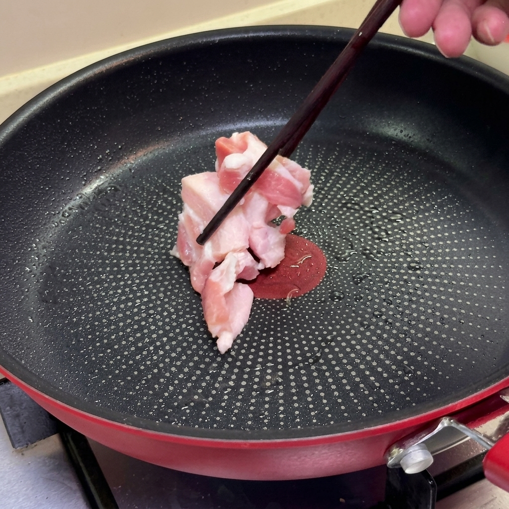 Bacchette che adagiano fette di pancetta di maiale cruda in una padella antiaderente calda.