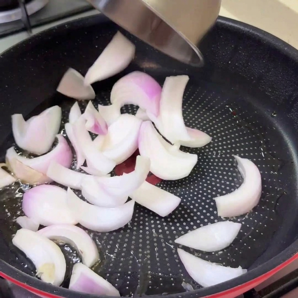 Cipolle crude affettate che vengono versate da una ciotola in una padella calda con lolio rilasciato dalla carne.