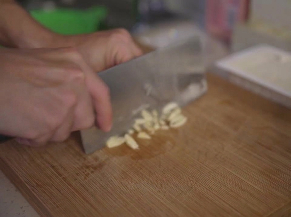 Aglio fresco tritato finemente su un tagliere di legno con un coltello da cucina.
