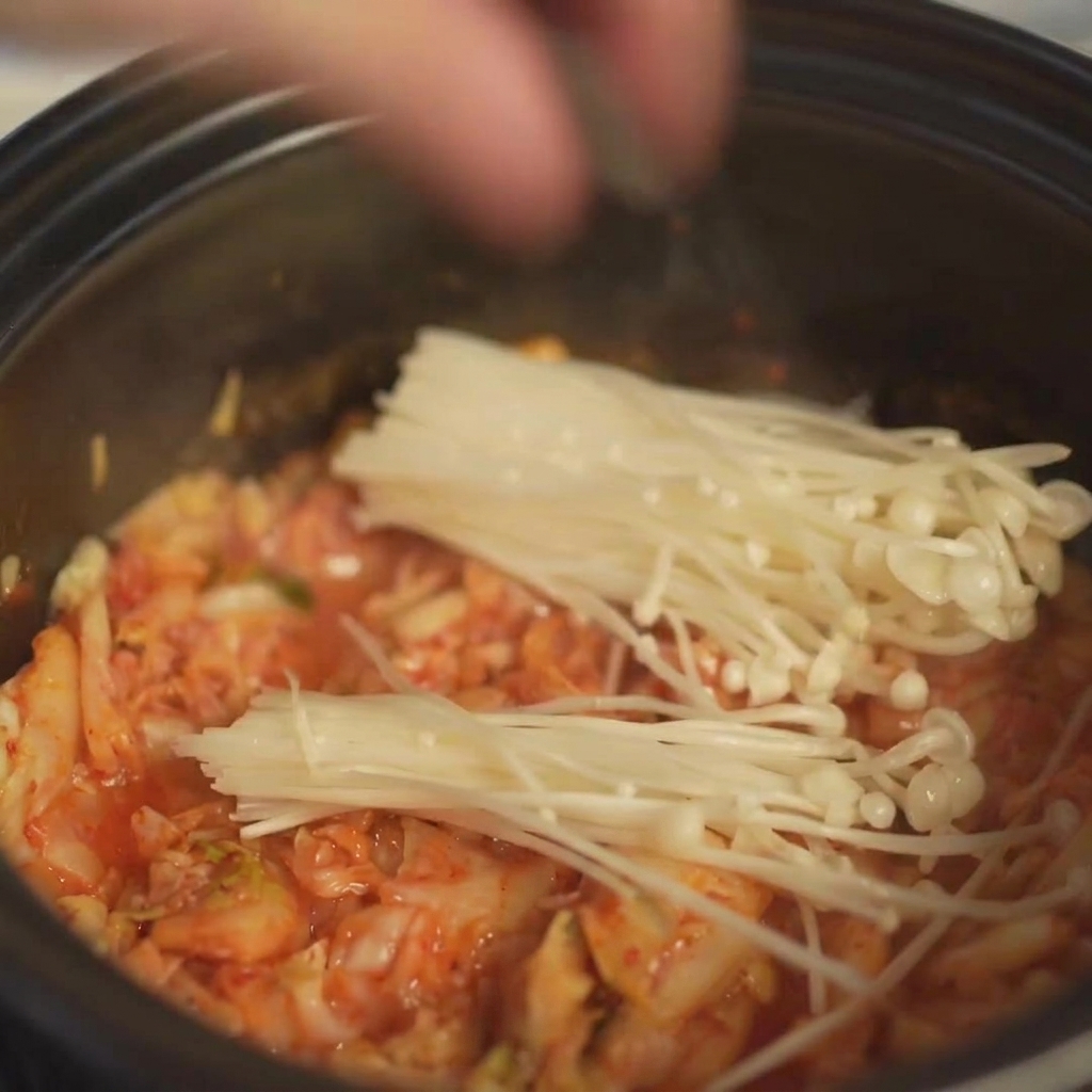 Disposizione di un mazzetto di funghi enoki freschi nella pentola sopra lo strato di kimchi.
