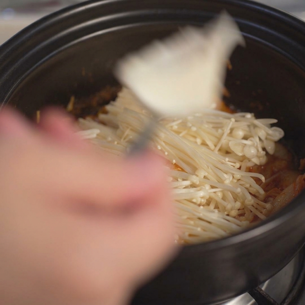 Grandi pezzi di tofu bianco morbido aggiunti nella pentola usando un cucchiaio.