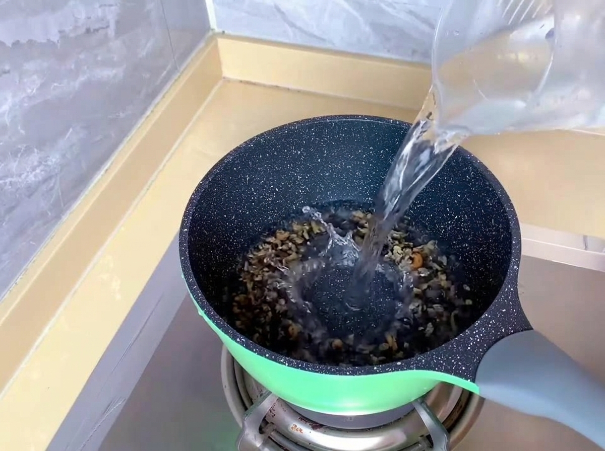 Acqua limpida versata da un misurino di plastica in una pentola verde su un fornello a gas.