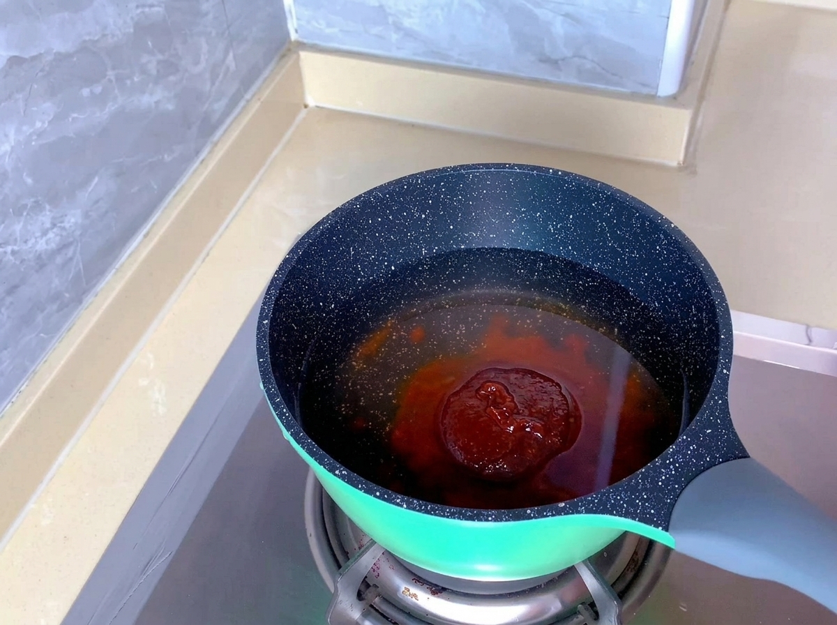 Un blocco di pasta di condimento per kimchi rossastra immerso in acqua limpida allinterno di una pentola.