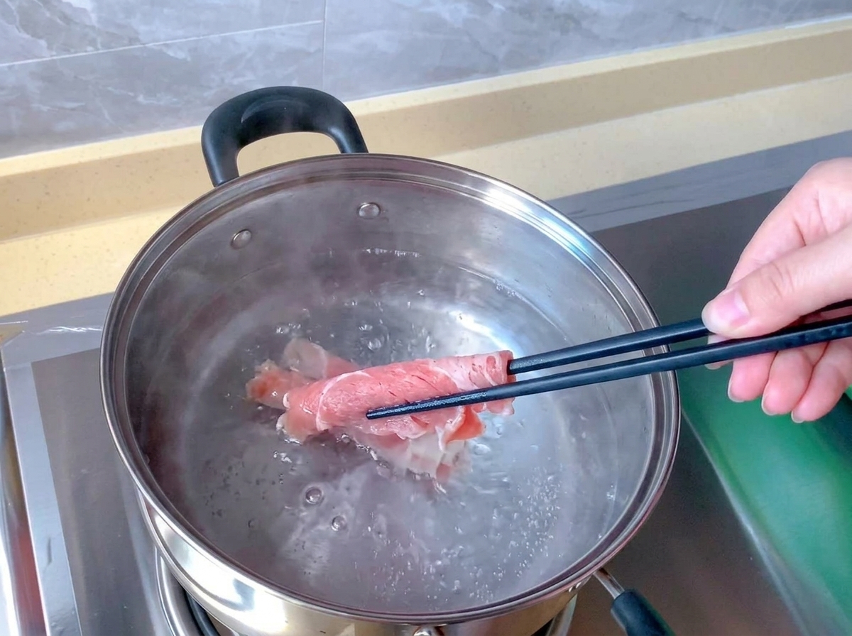 Delle bacchette immergono un involtino di manzo crudo e rosa in una pentola dacciaio con acqua bollente.