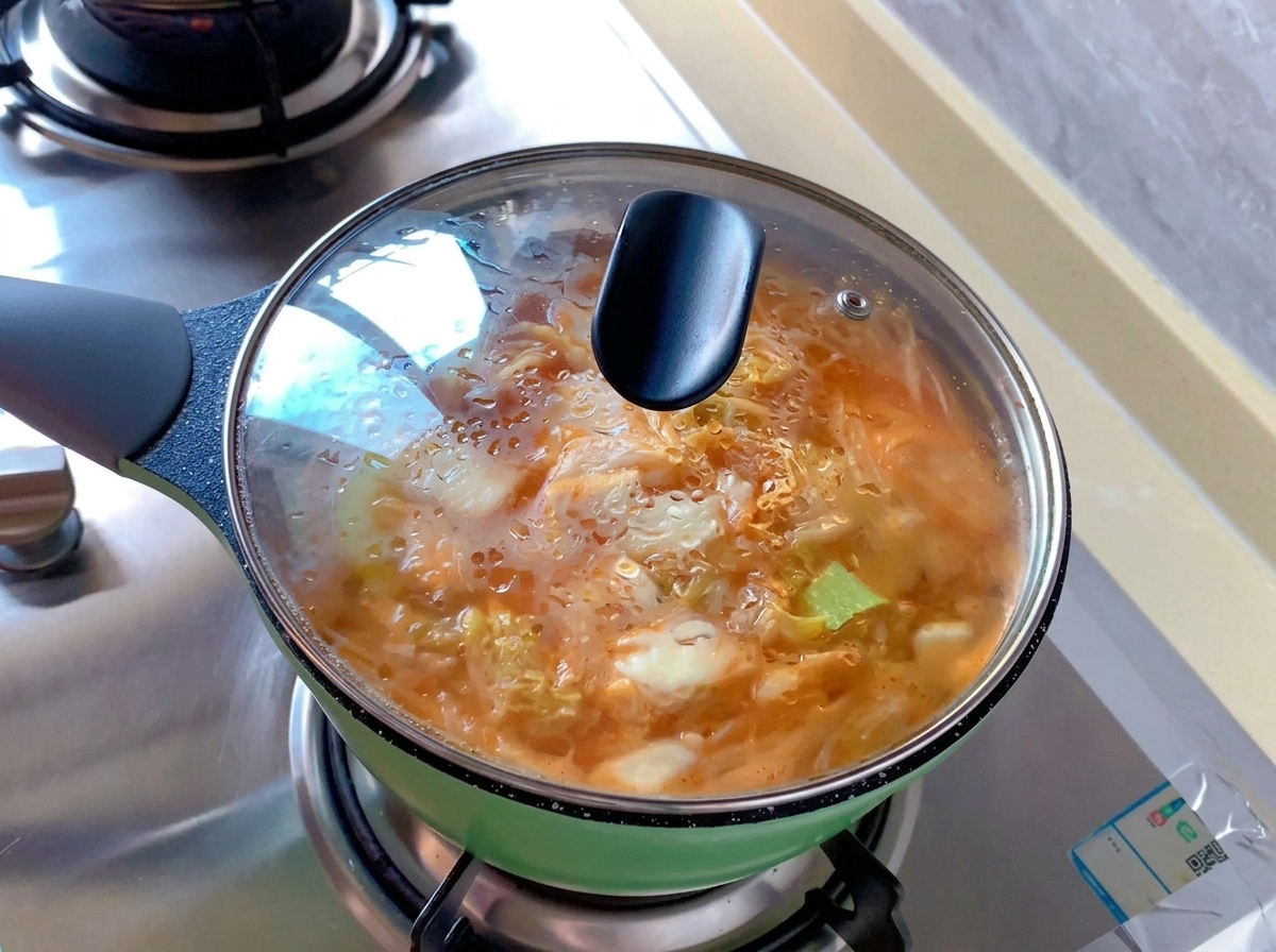 Una piccola pentola verde piena di zuppa di kimchi arancione coperta da un coperchio di vetro... con condensa di vapore.