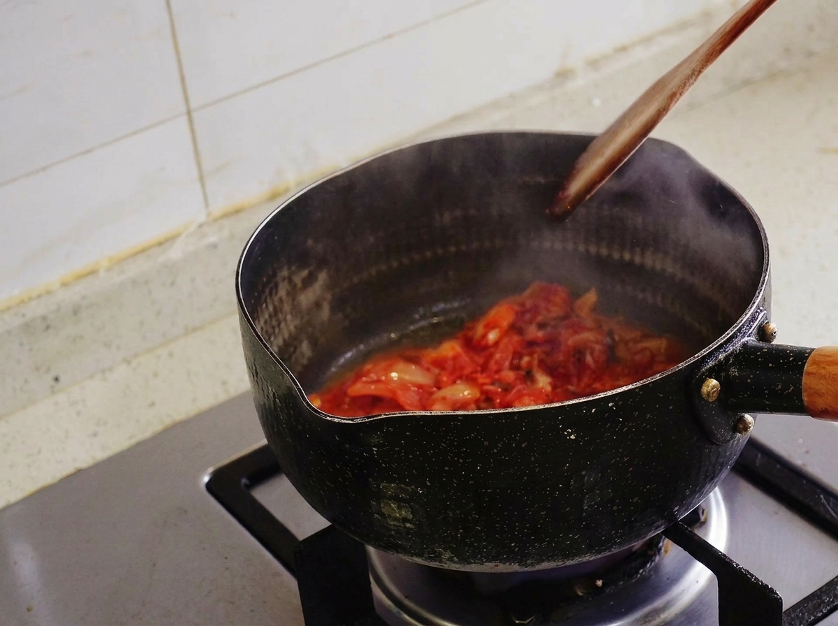 Kimchi saltato con una spatola di legno in una pentola nera, con vapore che sale.