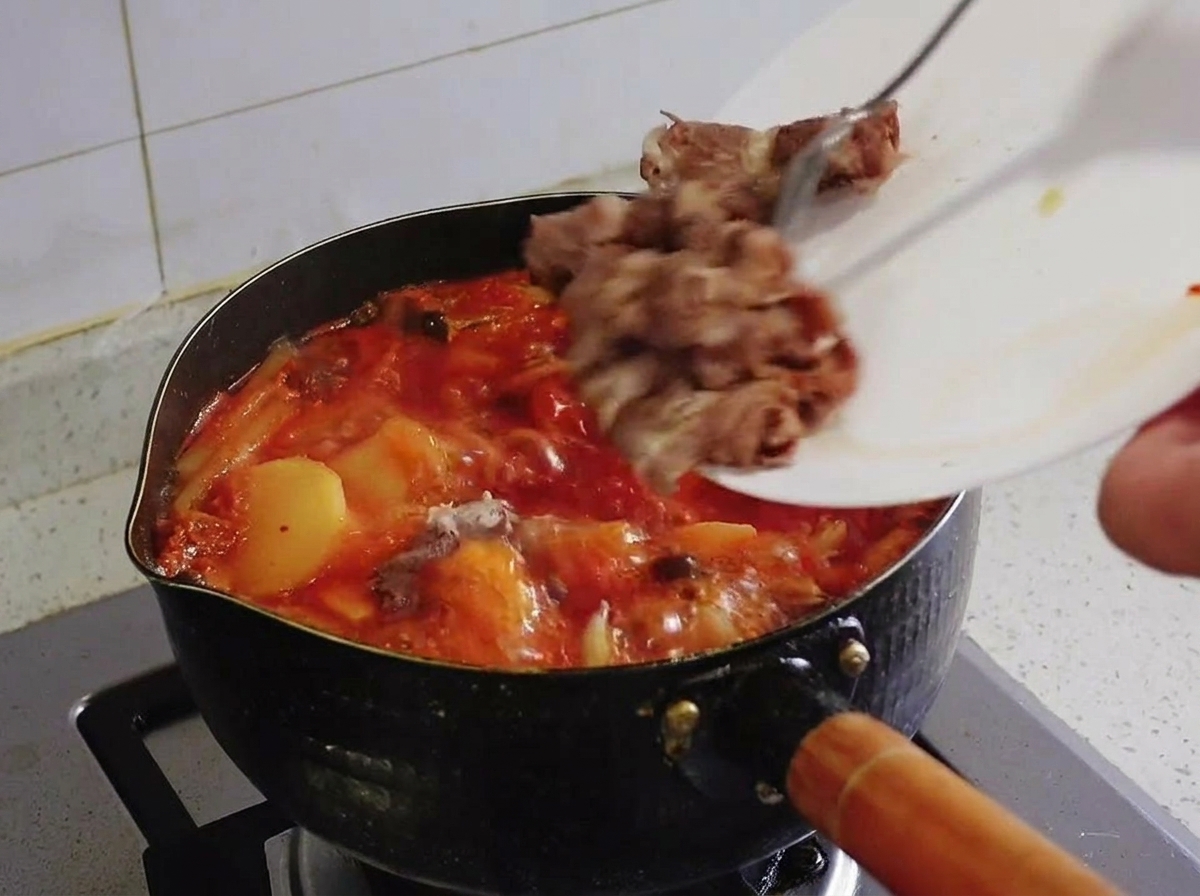 Pezzi di manzo sbollentati fatti scivolare da un piatto bianco in una pentola di stufato di kimchi rosso in ebollizione.