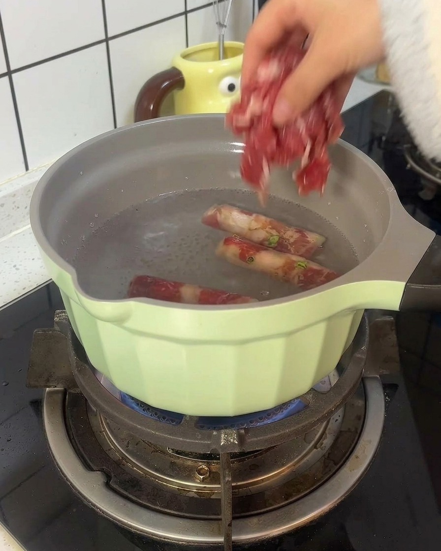 Involtini di manzo che sbollentano in una pentola verde chiaro con acqua bollente.