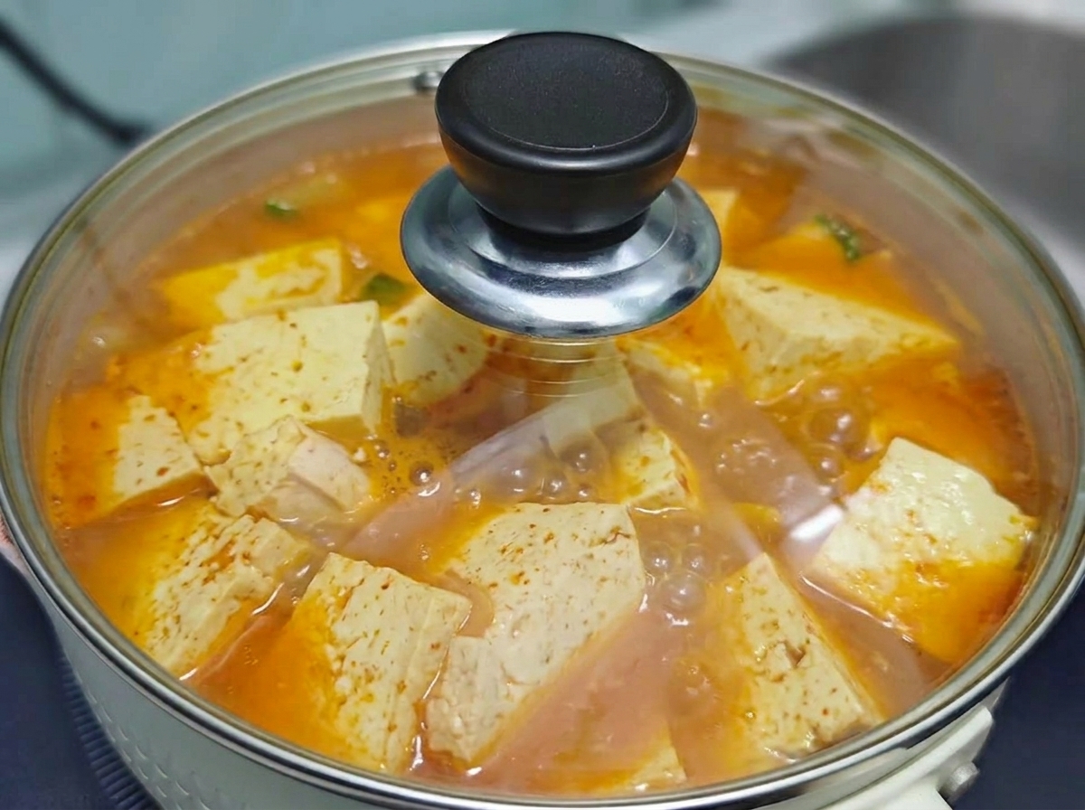 Un coperchio di vetro trasparente che copre la pentola di zuppa coreana di kimchi, manzo e tofu che bolle sul fuoco.