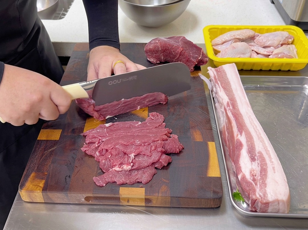 Taglio sottile di manzo crudo controfibra su un tagliere di legno con un coltello da chef.