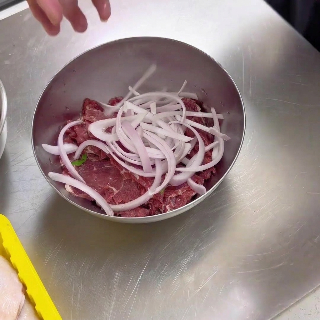 Fette di manzo crudo fresco allinterno di una ciotola di metallo condite con una manciata di cipolle bianche appena affettate.