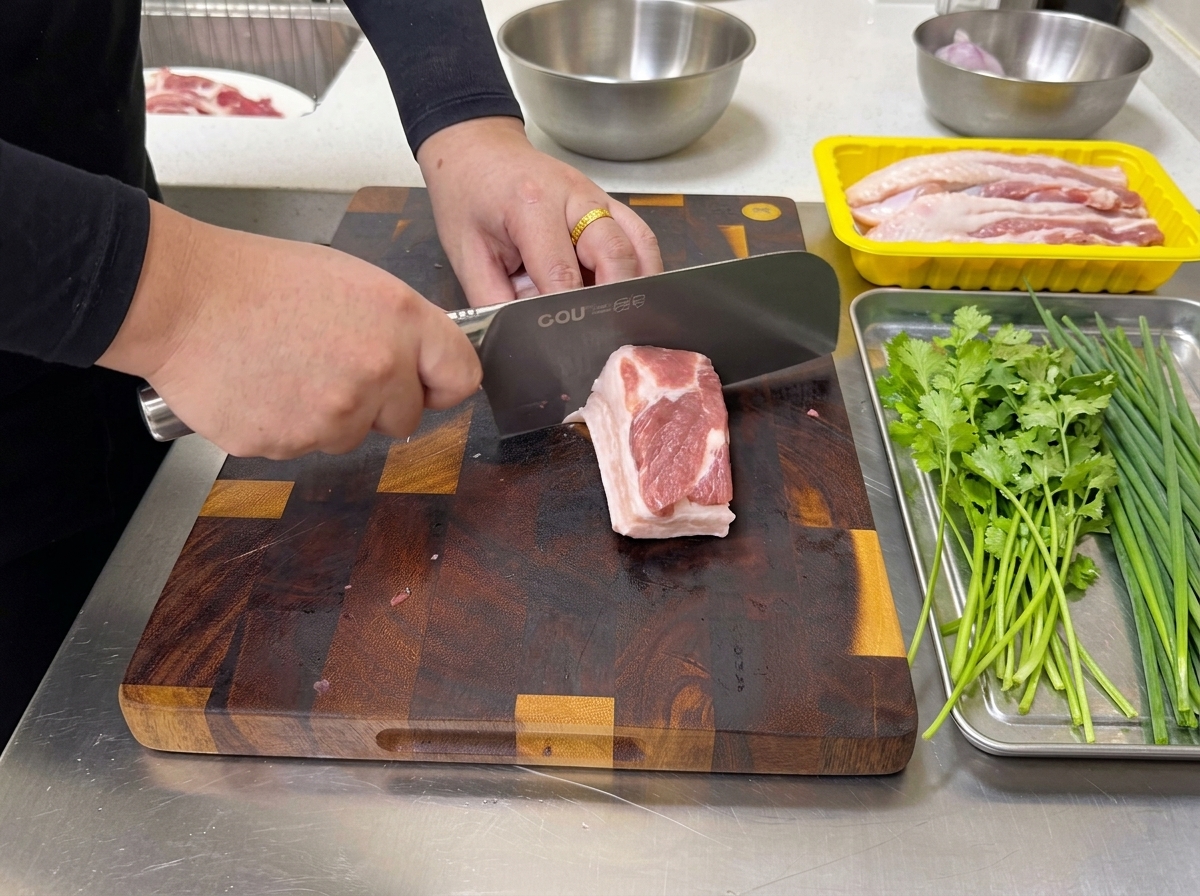 Una persona usa un grande coltello da cucina per tagliare un blocco di pancetta di maiale cruda a strati in strisce sottili su un tagliere.