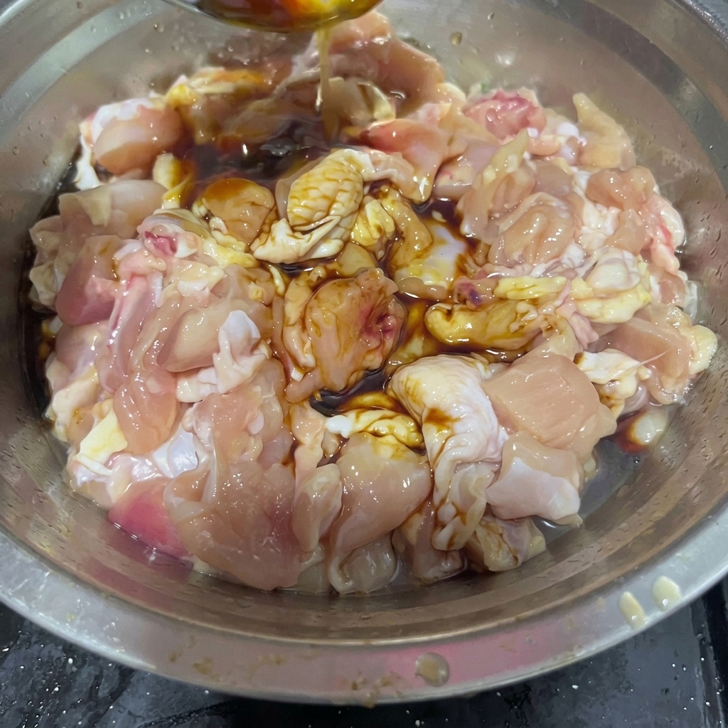 Vino da cucina versato da un cucchiaio dacciaio in una ciotola con pezzi di pollo crudo e salse scure.