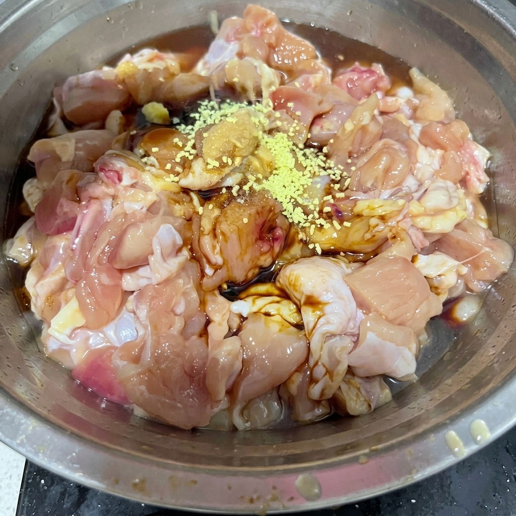 Brodo di pollo in polvere giallo e sale bianco spolverati sopra i pezzi di pollo crudo in una ciotola di metallo.