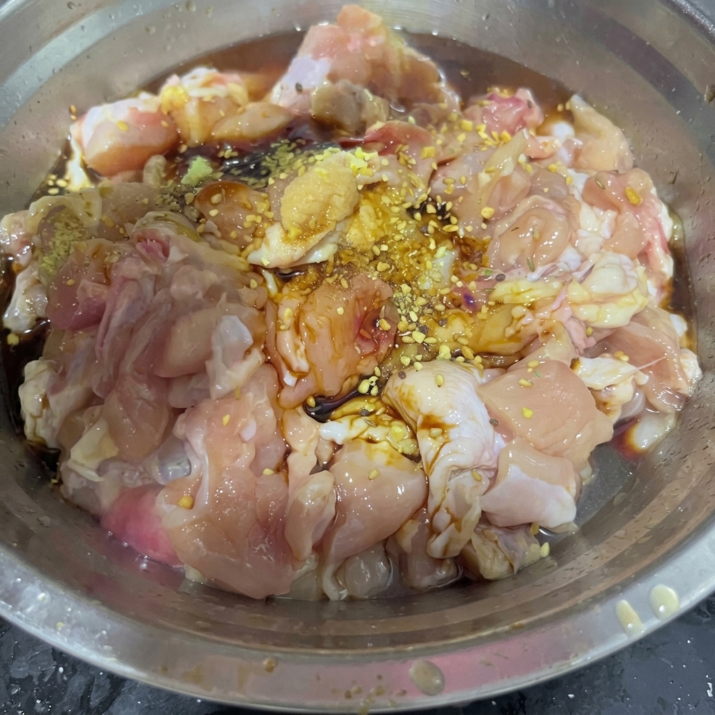 Un cucchiaio di miscela di spezie secche per barbecue distribuito sui pezzi di pollo marinati in una ciotola dacciaio.