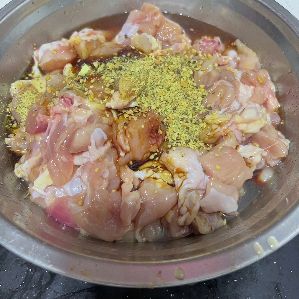 Zucchero semolato bianco spolverato sulla miscela di sovracosce di pollo condite in una ciotola dacciaio.