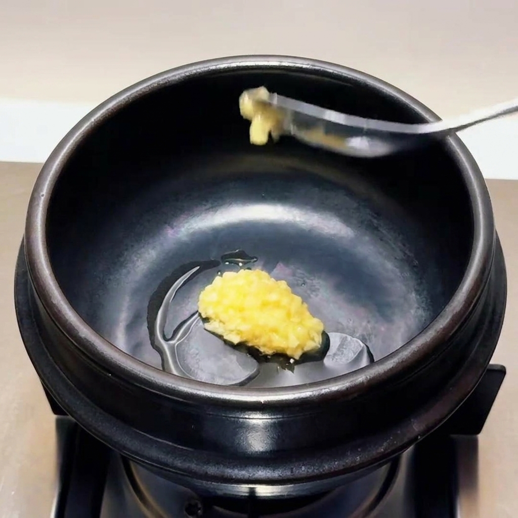 Un cucchiaio di aglio finemente tritato che viene calato e inserito nellolio caldo allinterno di una pentola di pietra nera.